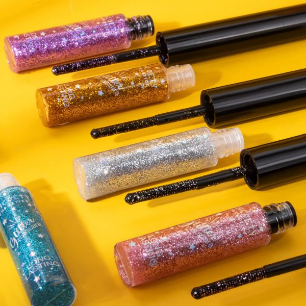 Glitter mascara tubes in purple, gold, silver, pink, and blue with black wands, arranged on a yellow background.