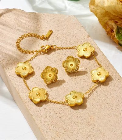 A beautifully arranged golden floral jewelry set, comprising a bracelet and earrings, resting on a beige stone, evoking a sense of luxury and refinement.
