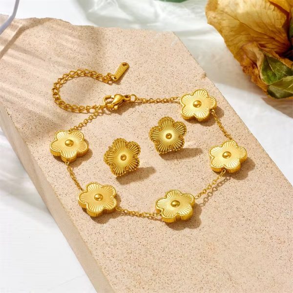 A beautifully arranged golden floral jewelry set, comprising a bracelet and earrings, resting on a beige stone, evoking a sense of luxury and refinement.
