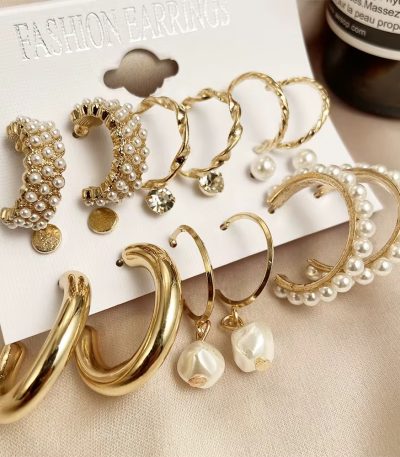 A set of 8 pairs of gold and pearl earrings on a white card, perfect for adding a touch of elegance to any outfit.