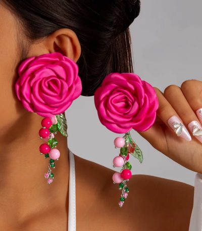 A close-up of a woman wearing vibrant pink rose earrings with beaded floral accents, adding a touch of luxury to her overall look.