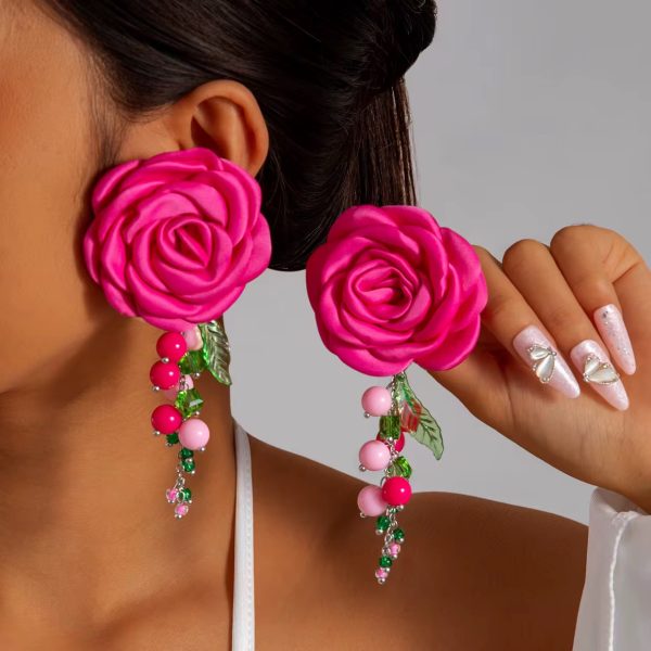 A close-up of a woman wearing vibrant pink rose earrings with beaded floral accents, adding a touch of luxury to her overall look.