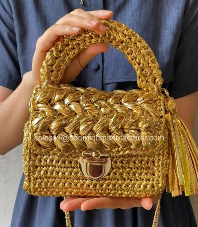 A luxurious golden woven crochet purse with a beautiful tassel, held by a woman in a blue dress, showcasing its elegant design and craftsmanship.