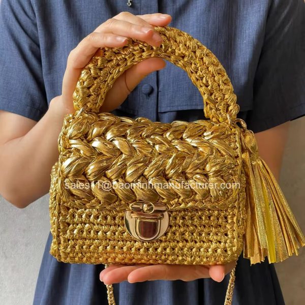 A luxurious golden woven crochet purse with a beautiful tassel, held by a woman in a blue dress, showcasing its elegant design and craftsmanship.