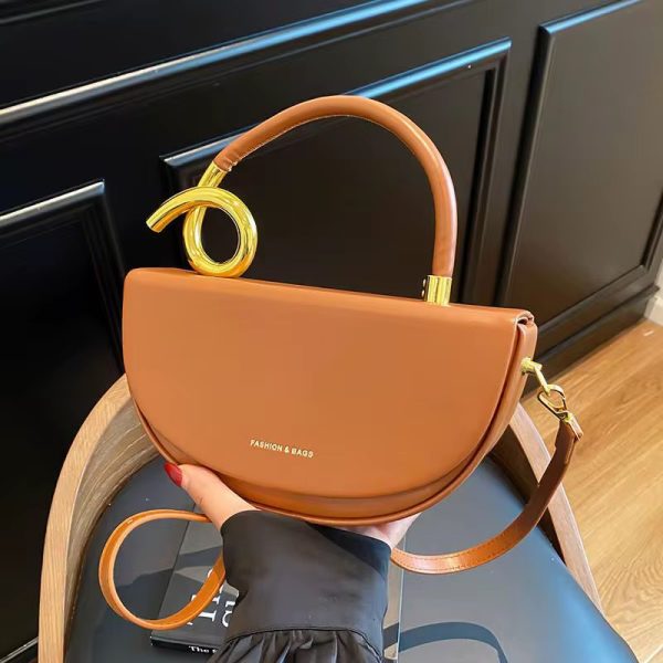 A luxurious brown half moon shoulder bag with gold accents, held by a woman's hand, showcasing its sleek design and sophisticated style.