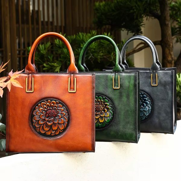 Three luxurious leather handbags in brown, green, and black, adorned with intricate floral embellishments, placed on a white surface amidst lush greenery.